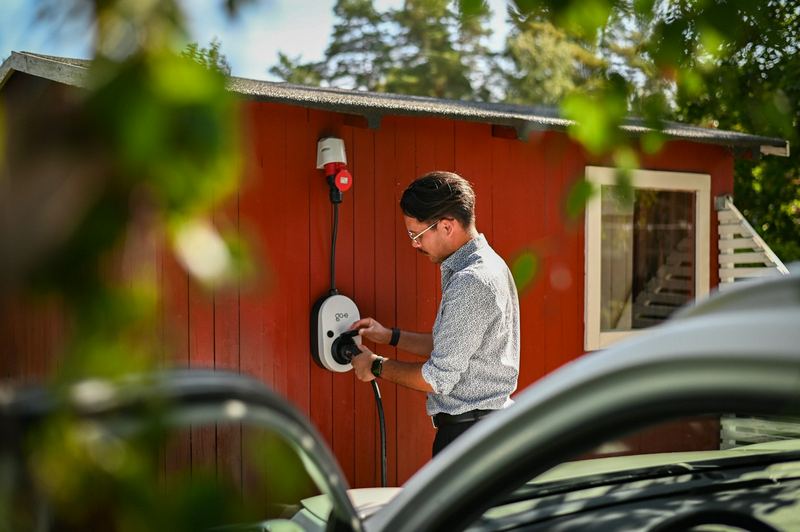 A man plugging a charging cable into a wall box mounted on a shed at home