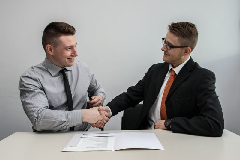 Two people shaking hands across a table with signed paperwork open between them