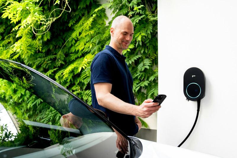 A man beside his electric car, looking at his phone next to a home charger